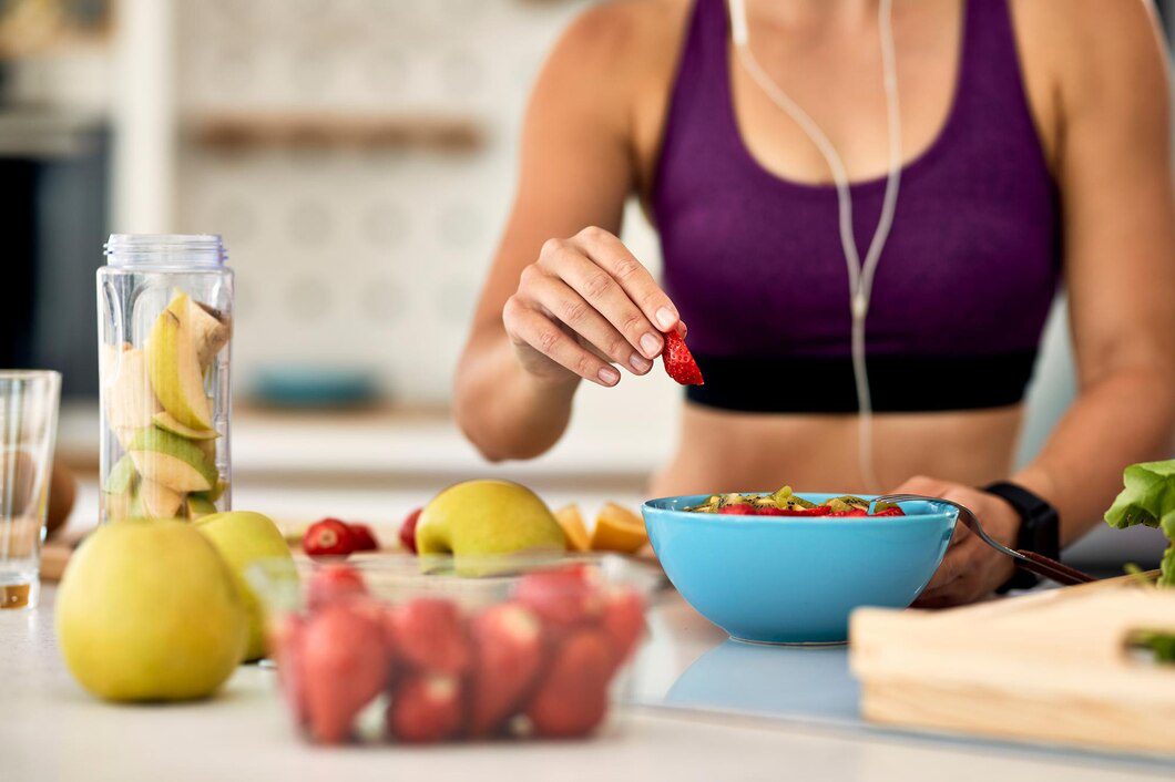 Primer plano de una mujer atlética añadiendo fresas mientras prepara una ensalada de frutas en la cocina